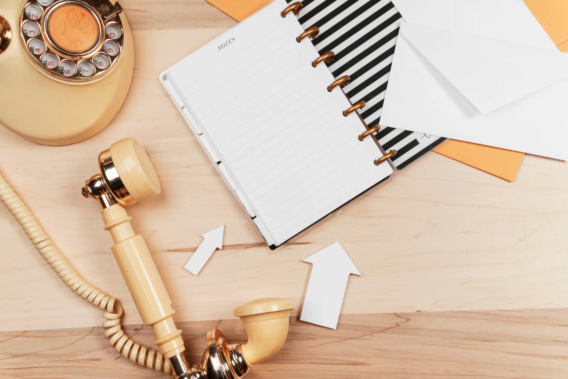 Vintage rotary phone with open notebook, envelopes, and arrow cutouts on a wooden desk — get in touch with us